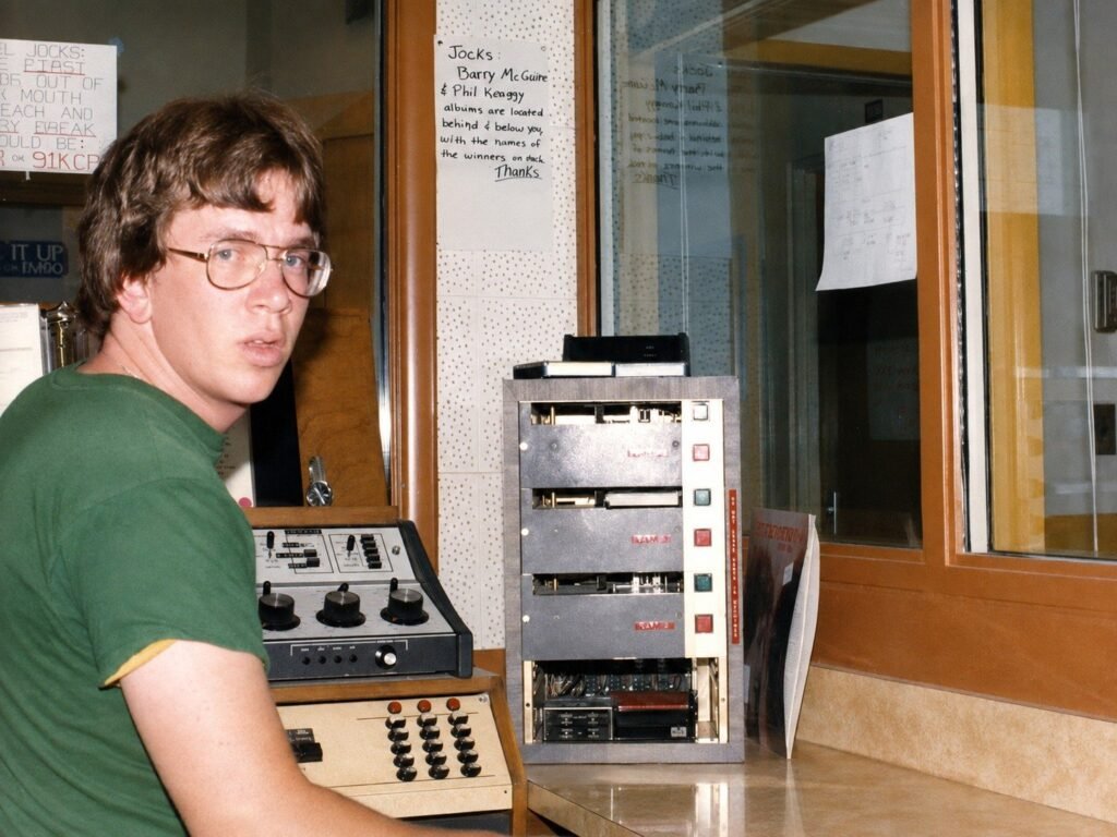 KCPR DJ beside the broadcast cart machine and studio controls