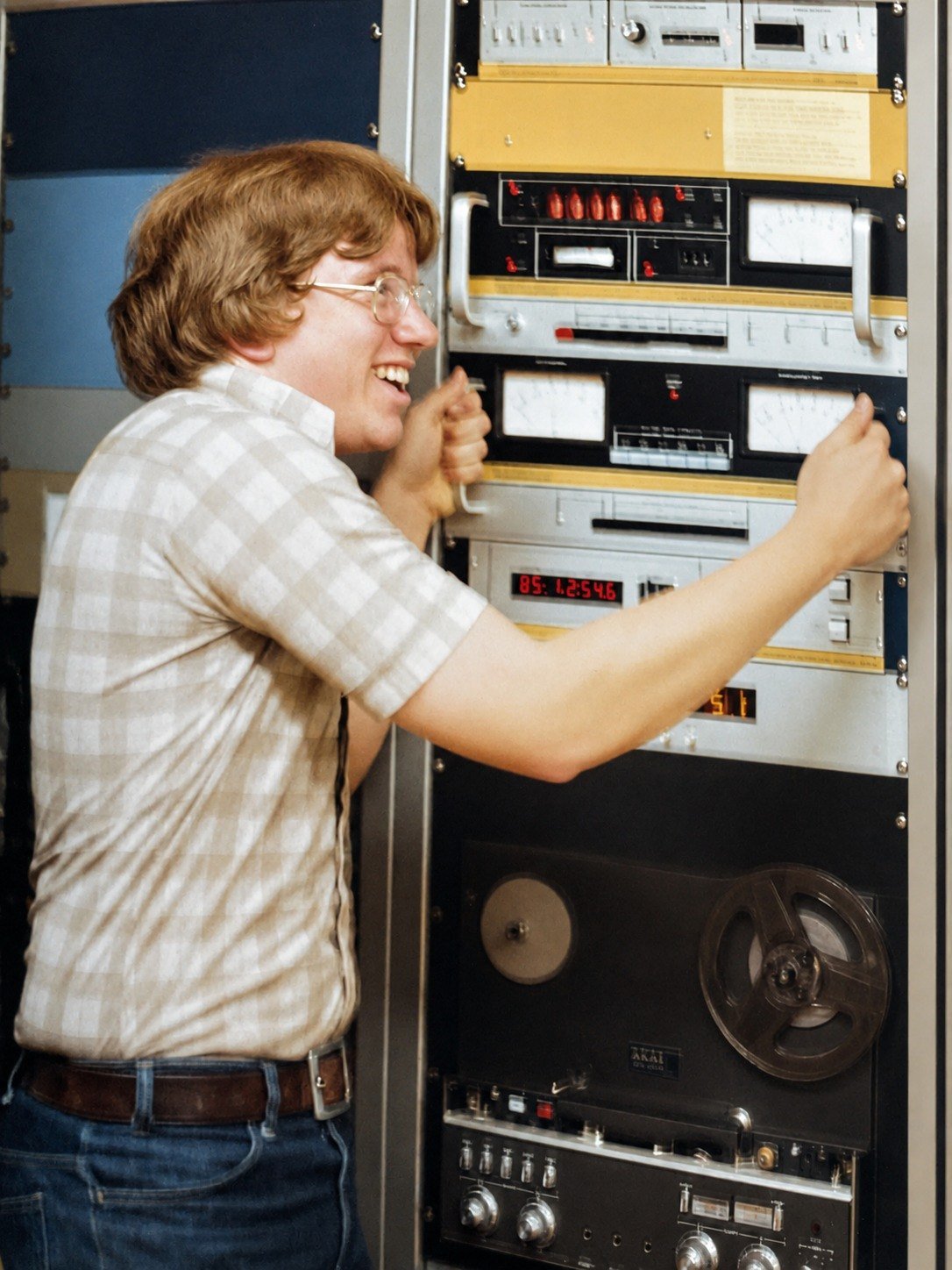 KCPR DJ beside the station equipment rack and reel-to-reel recorder