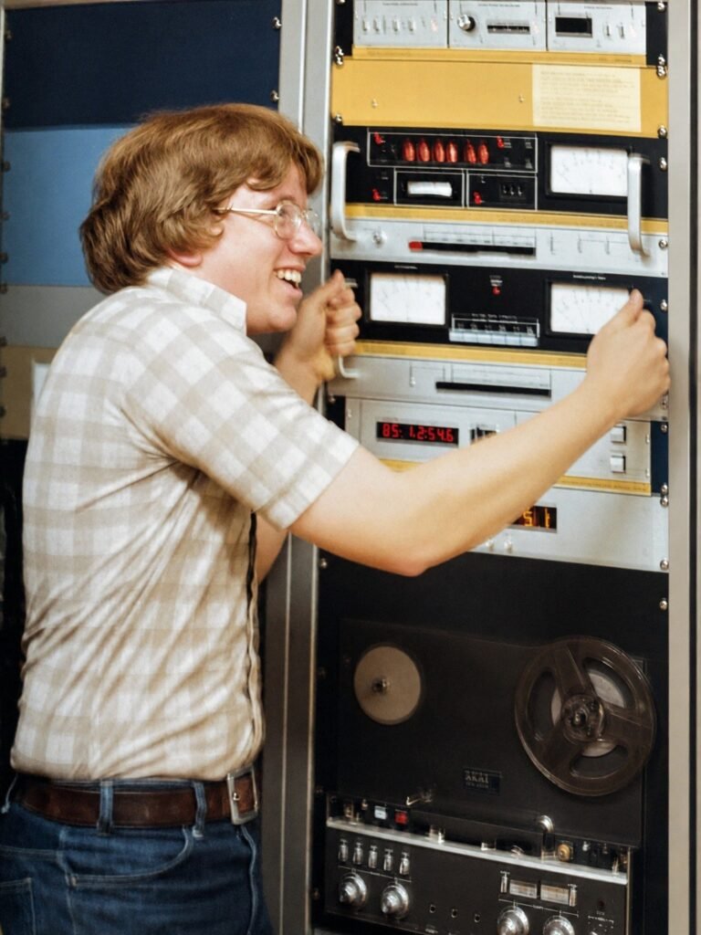 KCPR DJ beside the station equipment rack and reel-to-reel recorder