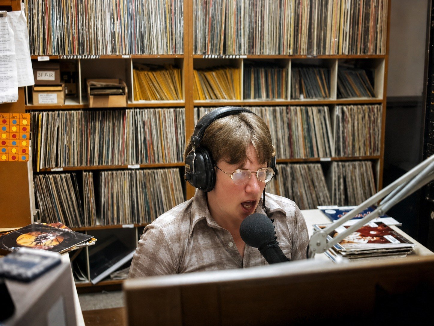 KCPR DJ on the air in the Cal Poly radio studio with shelves of LP records behind him